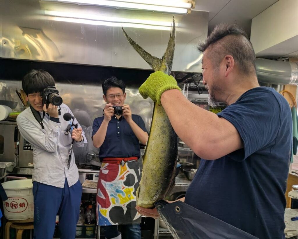 魚の伝道師こと上田勝彦さんが魚さばき手袋を着用してシイラをさばく様子を一緒に取材しました。左が水産新聞の市川記者です。